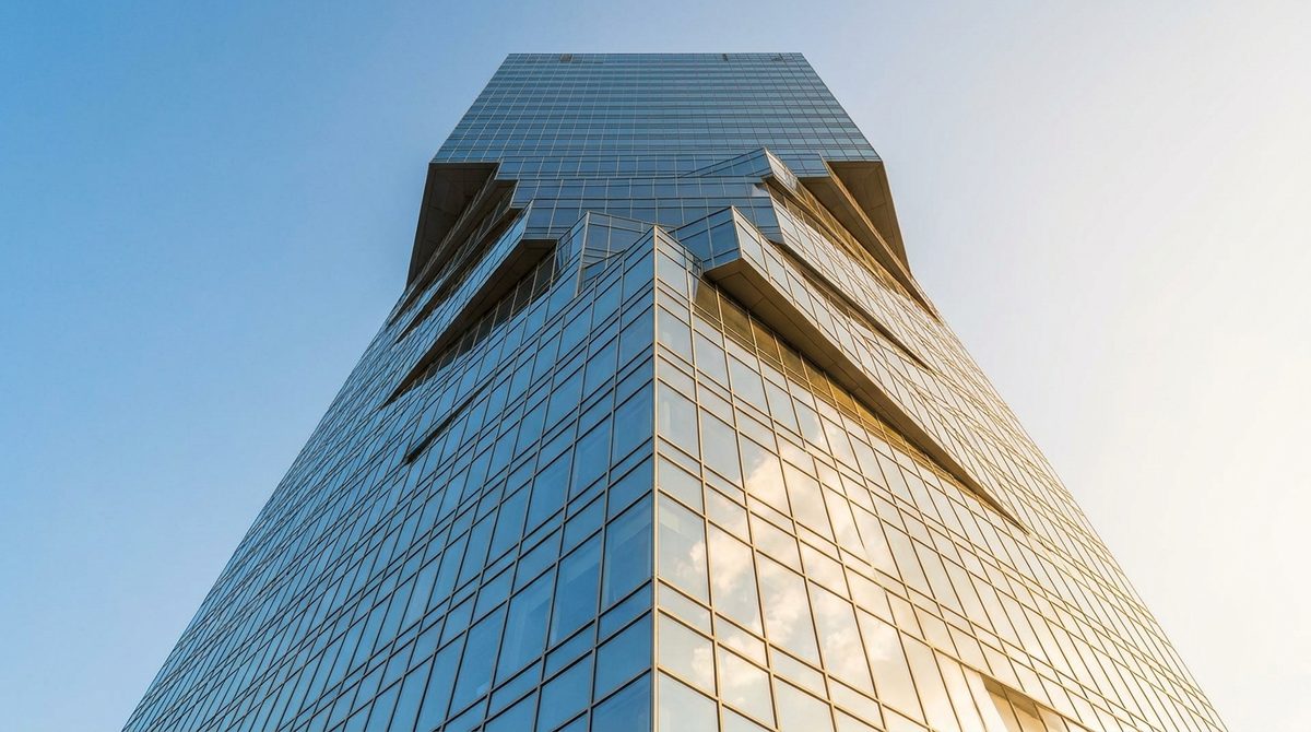 A modern high-rise glass office tower viewed from below against a clear sky